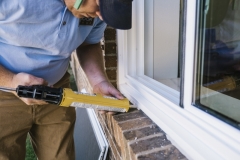 Worker applying sealant during window installation process for The Window & Door Store project.